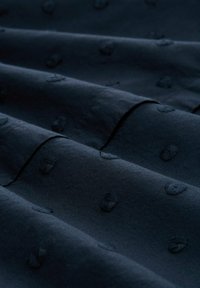Dark blue textured fabric with subtle, raised circular patterns, featuring soft, smooth drapes and a consistent color throughout.