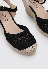 Sandales compensées en espadrille noires tissées, avec un bout ouvert, présentant une couverture au crochet pour les orteils et une sangle à la cheville. Tige texturée et semelle en jute naturel.