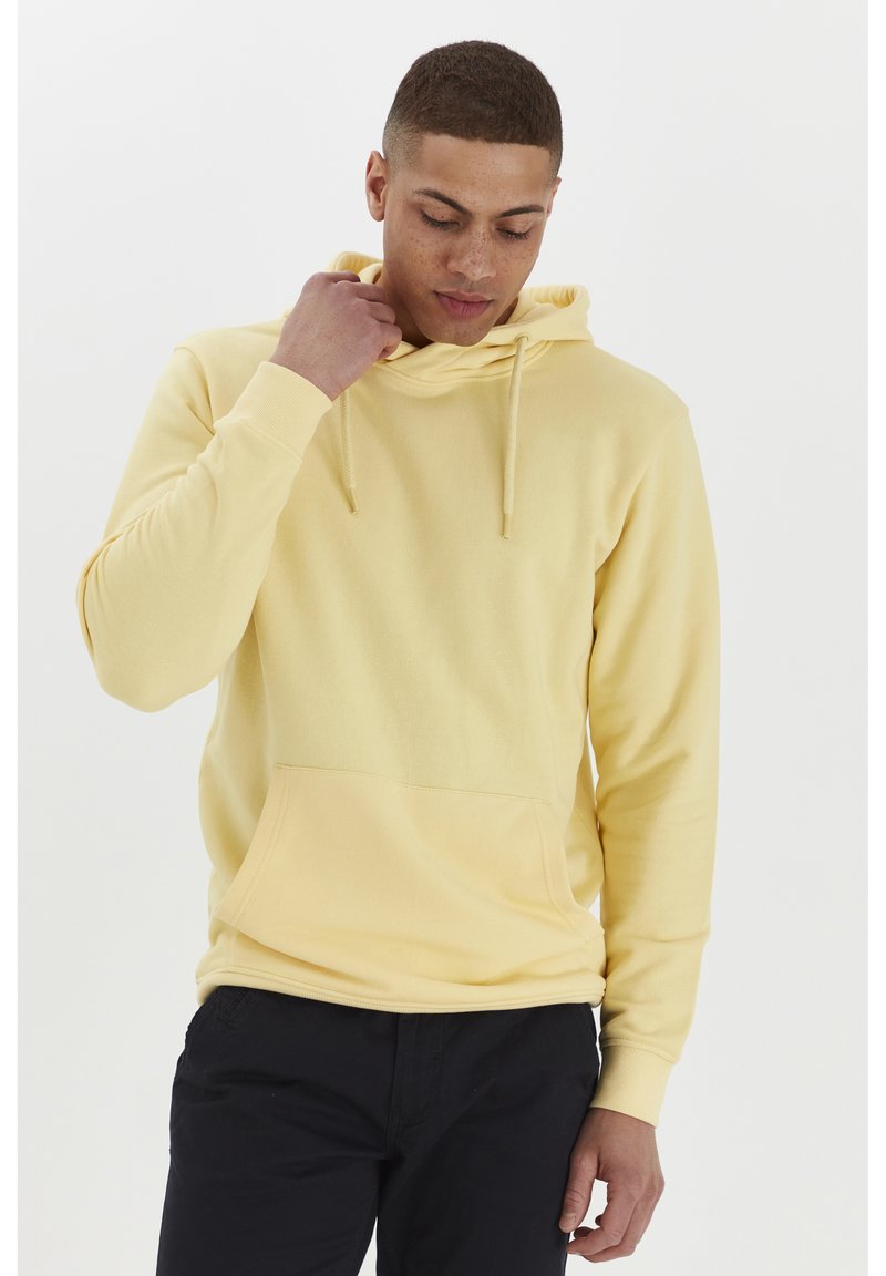 Geel hoodie van zacht materiaal, met een voorkrui pocket, verstelbare trekkoordkap en geribbelde manchetten. Draagt met donkere broek.
