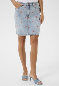 Jupe en denim bleu clair avec broderie de cerises rouges. Présente une coupe ajustée, un design à cinq poches et une fermeture à boutons sur le devant.