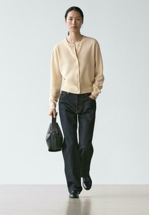 Lys beige uldcardigan med knapper, kombineret med mørkeblå denimjeans. Holder en sort lædertaske med en glat tekstur og enkelt design.