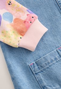 Lichtblauw denimstof met een roze geribde boord en een kleurrijke dierenprint. Inclusief een zichtbare zak met roze stiksel.