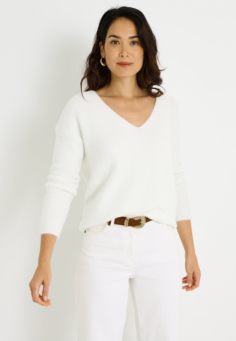 Suéter blanco y esponjoso con cuello en V y mangas largas; combinado con pantalones blancos y un cinturón marrón. Diseño minimalista y textura suave.