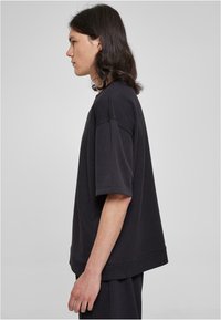Černé oversized tričko s krátkým rukávem, vyrobené z měkké látky. Má kulatý výstřih a volný střih, stylizované s delším zadním lemem.