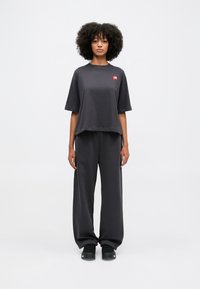 T-shirt oversize grigio scuro a maniche corte con un patch logo rosso, abbinata a pantaloni larghi grigio scuro e calzature nere.