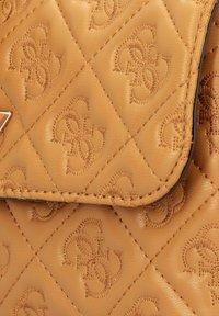 Gesteppte Handtasche aus beige Leder mit geprägtem Logomuster, mit einer Klappe als Verschluss und kontrastierenden Steppnähten. Luxuriöses Finish und Textur.