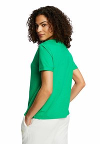 Camiseta verde de manga corta hecha de tela suave, con cuello redondo y un corte relajado con puños de manga enrollados.