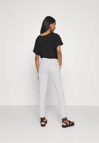 Haut noir à manches courtes avec un décolleté arrondi, associé à un pantalon ajusté gris clair et des sandales noires à lanières.