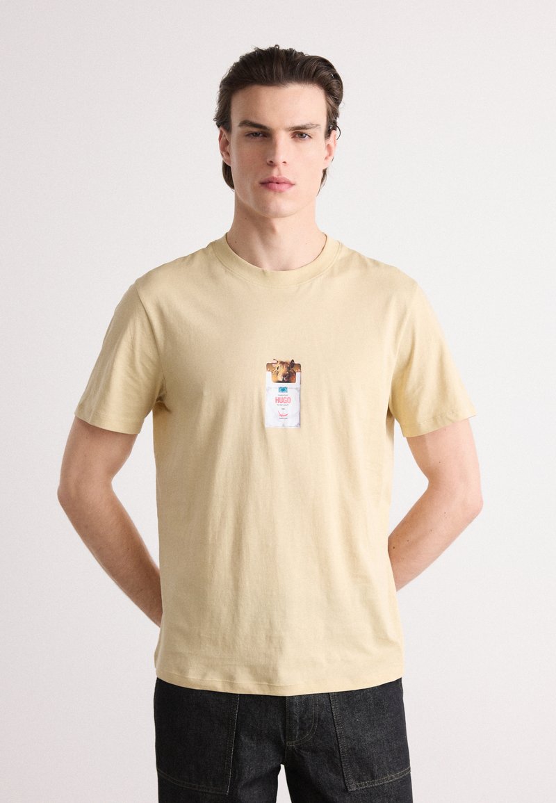 Beige bomulds T-shirt med rund hals, der har et grafisk design på brystet af en hund og et mærke med teksten "Hugo."