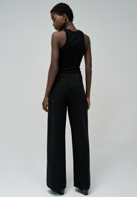 Top negro de tirantes combinado con pantalones anchos negros. El conjunto presenta un diseño ajustado y una textura suave, con un detalle mínimo.