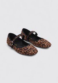 Une paire de chaussures plates Mary Jane avec un imprimé léopard, des bordures noires, et des sangles à boucle ajustables sur un fond neutre.