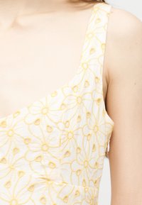 Gros plan sur une robe blanche sans manches avec des motifs floraux brodés jaunes sur le tissu.