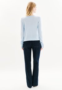 Lichtblauwe trui met lange mouwen gecombineerd met donkerdenim flared broek. De trui heeft een ronde hals en een zachte structuur, terwijl de broek een rechte snit heeft.