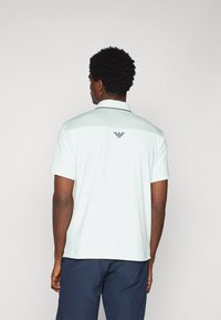 Φακελωτό μαντήλι σε ανοιχτό μέντα απόχρωση με κοντά μανίκια, διαθέτοντας υφασμάτινη πλάτη και μικρό λογότυπο σε σκούρα απόχρωση στον γιακά.