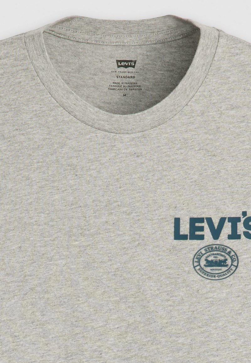 Camiseta de algodón gris con cuello redondo, con un logo de Levi's en azul y un emblema redondo de la marca impreso en la parte delantera.