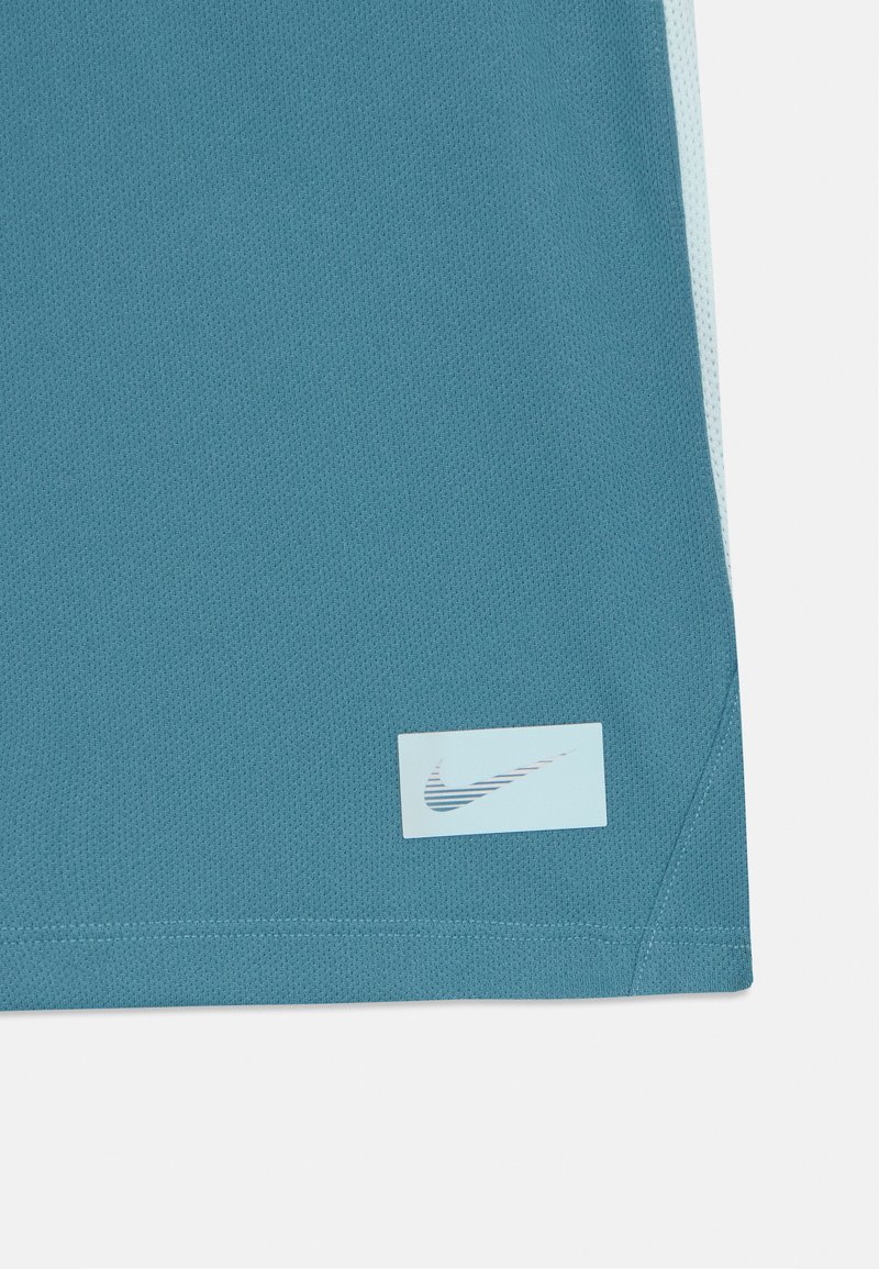 Maglietta sportiva turchese realizzata in tessuto traspirante, caratterizzata da una consistenza liscia. Include un logo Nike rettangolare azzurro chiaro sull'orlo.