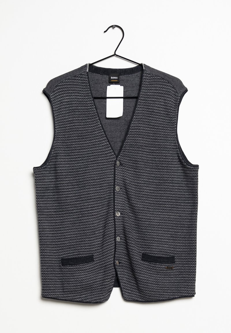 Tmavě šedá pletená bezrukávová vesta na knoflíky s texturovaným vzorem a dvěma předními kapsami visící na černém ramínku s bílou etiketou.