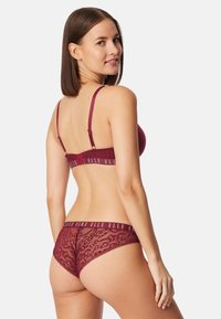 Bordeauxrode kanten beha en bijpassende hipsteronderbroek met een merkband. De bralette heeft dunne verstelbare bandjes en een gladde afwerking.