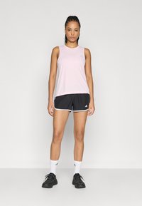 Ανοιχτό ροζ μπλουζάκι χωρίς μανίκια συνδυασμένο με μαύρο σόρτς με λευκές λεπτομέρειες· μοντέλο που φοράει μαύρα αθλητικά παπούτσια και λευκές κάλτσες με διακριτικά λογότυπα.