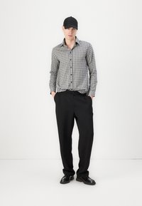 Grau und schwarz karierter Hemd mit Knöpfen, lockere schwarze strukturierte Hose, schwarze Mütze und schwarze Schuhe. Das Outfit hat eine entspannte Passform.