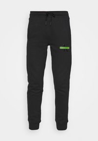 Pantalones deportivos negros de mezcla de algodón, con cinturilla elástica y cordón, bolsillos laterales y un parche de logo verde en la parte frontal.