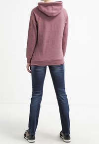 Felpa con cappuccio di un rosa tenue, realizzata in tessuto morbido, con polsini e orlo a coste. Abbinata a jeans blu scuro e scarpe da ginnastica nere.