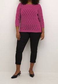Pull en maille rose avec un motif ondulé, manches trois-quarts ; assorti à un pantalon noir longueur cheville et des talons slingback noirs.