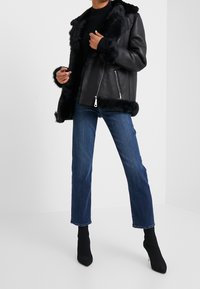 Svart skinnjacka med pälskant, med sjalkrage och två fickor med dragkedja. Matchad med blå korta jeans och svarta stövlar med klack.