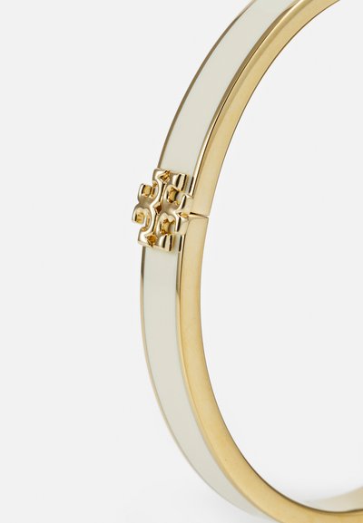 Bangle käevõru on valmistatud kuldse metallist alusest, millel on sile kreemjas viimistlus ja dekoratiivne klipp, millel on detailne muster.