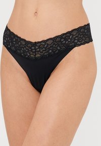 String en dentelle noire avec une large ceinture en dentelle. Le matériel principal est lisse et extensible, mettant en valeur de délicates détails floraux en dentelle en haut.