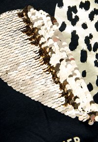 Decorazione in paillettes dorate e argentate su tessuto nero con motivo a stampa leopardata. Le paillettes hanno una texture liscia e lucida.