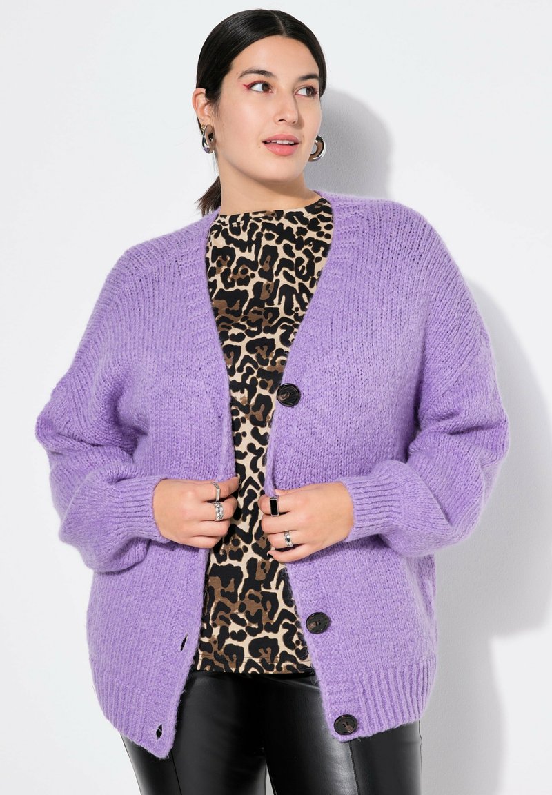 Lavendelfarbene Strickjacke im Oversized-Schnitt mit Knopfverschluss und gerippten Bündchen. Getragen über einem leo-musternden Oberteil und schwarzen Kunstlederhosen.