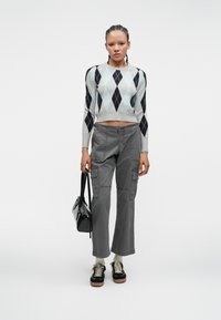 Sweater gris court avec un motif losangé noir et bleu clair, pantalon cargo gris avec poches, sac noir et baskets noires avec des accents beiges.