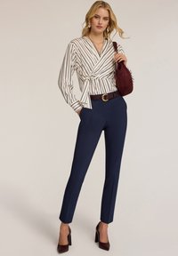 Bílo-modře pruhovaná zavinovací blůza, námořnické kalhoty na míru, hnědý texturovaný opasek se zlatou sponou, vínová kabelka a boty na vysokém podpatku.