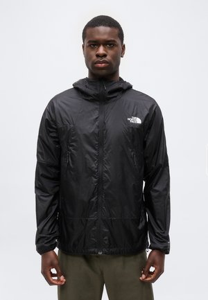 Άνδρας που φοράει μαύρο μπουφάν The North Face με φερμουάρ και κουκούλα, στέκεται μπροστά σε απλό λευκό φόντο.