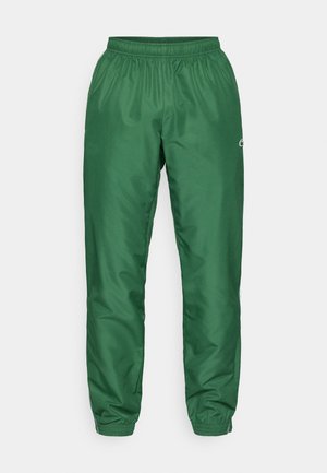 Pantalones deportivos verdes con cinturilla elástica, tobillos ajustados y tejido liso y brillante. Detalle sutil del logo en la pierna.