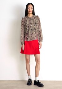 Bluză cu mâneci lungi, cu model floral în tonuri calmate, asociată cu o fustă A-line roșie strălucitoare. Încălțămintea constă în mocasini negri cu șosete albe.