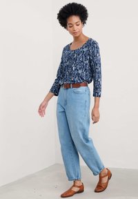 Granatowa bluzka z nadrukiem liści, okrągłym dekoltem i długimi rękawami, w połączeniu z jasnoniebieskimi dżinsami z wysokim stanem i brązowymi plecionymi butami.