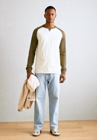 Pikad varrukad, oliivroheline ja valge raglan-särk, helesinised teksad ja beež jakk, mida hoitakse ühes käes. Spordijalatsid roheliste aktsentidega.