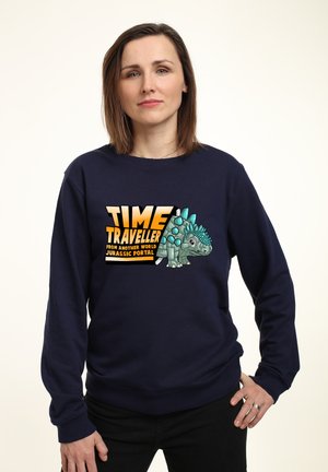 Námořnická modrá mikina s grafikou stylizovaného dinosaura a textem "ČASOVÝ CESTOVATEL z jiného světa, JURASSIC PORTAL."