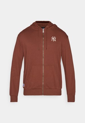 Hanorac crem cu fermoar, confecționat dintr-un material moale, având un buzunar tip cangur, glugă cu șnururi și un logo alb al echipei New York Yankees pe piept.
