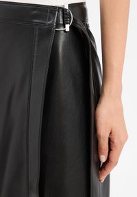 Jupe en cuir noir avec une taille ajustée, dotée d'un anneau en métal et d'un design minimaliste. La texture est lisse avec des détails de couture subtils.