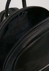 Le sac à dos en cuir noir présente un extérieur texturé, des compartiments à double zip et un intérieur en tissu lisse avec une poche zippée et des détails de logo.