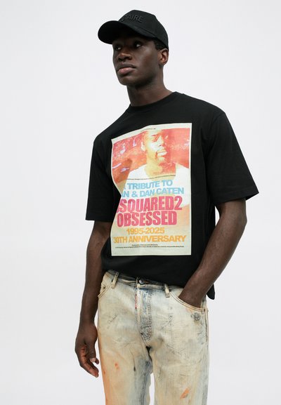 Tricou negru cu un imprimeu grafic colorat și text pentru cea de-a 30-a aniversare a DSquared2; purtat cu blugi ușor deteriorați. Căciulă neagră.