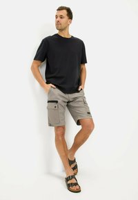 Herre sort t-shirt med korte ærmer, parret med lysegrå cargo shorts med flere lommer og en sort lynlås-accent, båret med brune sandaler.