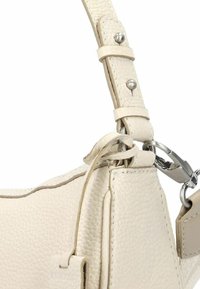 Borsa a mano in pelle crema in primo piano, con superficie testurizzata, tracolla regolabile con accessori in argento e dettagli cuciti lungo i bordi.