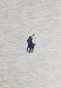 Broderad marinblå polo spelare på häst med upplyft klubba på ljusgrått stickat tyg.