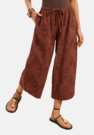 Brown wide-leg cropped pants with floral pattern and drawstring waist, worn with black sandals featuring white shell decorations.