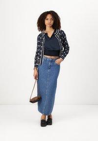 Navy patterned cardigan with white accents, black top, long blue denim skirt, and black shoes. Carrying a small brown handbag.
