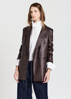 Blazer double boutonnage en cuir marron avec revers châle, comportant deux boutons, des coutures verticales et une texture lisse. Porté par-dessus une chemise blanche.